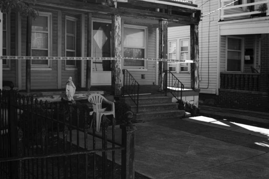 A black and white photo of a house with its front porch cordoned off with police crime scene tape, representing types of murder in Canada