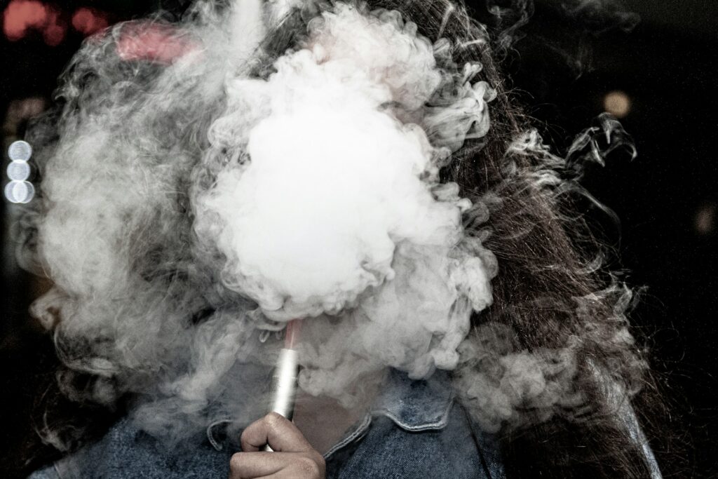 Person holding a shisha and blowing out smoke with the smoke covering their face.