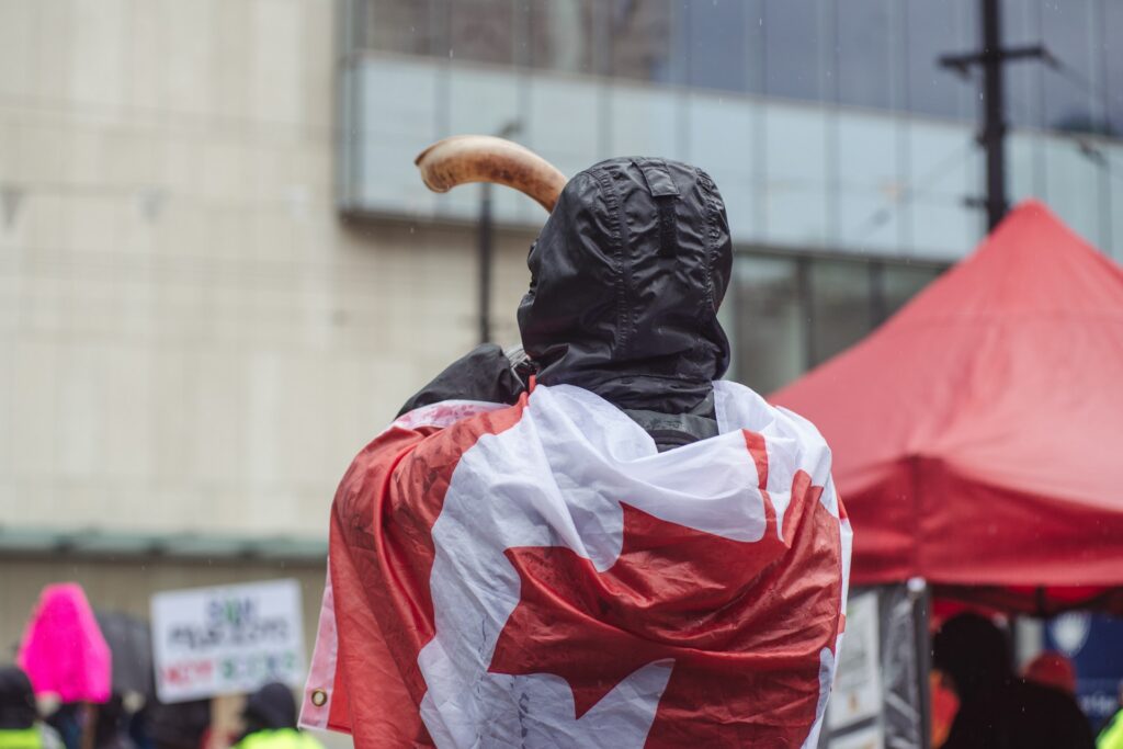A person with a Canada flag wrapped around shoulders at a public protest, representing Canada's new hate crime laws and what Bill C-9 means for criminal cases in Canada.