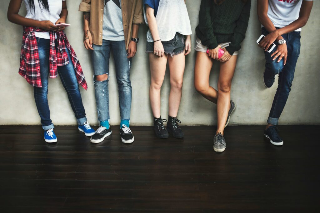 A group of young people leaning against a wall, some holding cellphones, representing cyberbullying, sexting and youth criminal charges.